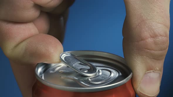 Male Hand Opening a Shaken Can of Beer on a Blue Background