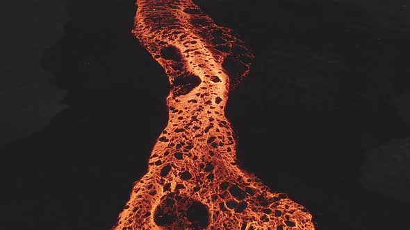 Drone flying over meandering river of glowing lava, Iceland. Aerial forward