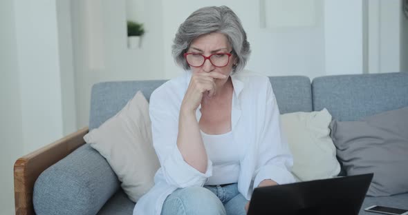 Thoughtful Senior Female Blogger Using Laptop for Writing Posts in Social Network
