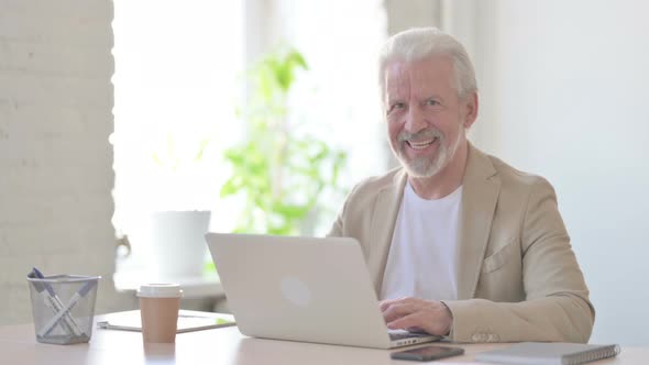 Old Man Smiling at Camera While Using Laptop in Office