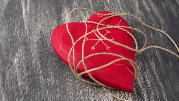 Red wooden heart entangled in a rope on a gray wooden background