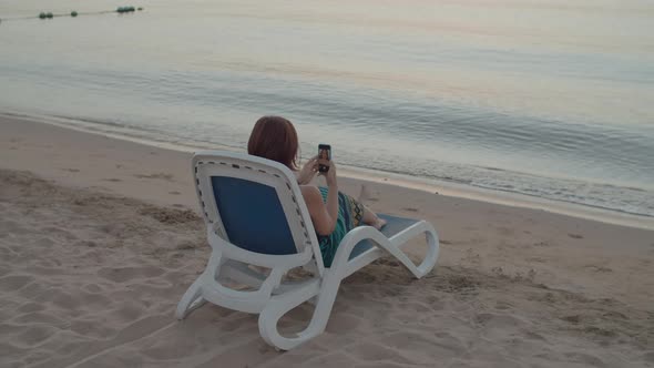 Woman Taking Selfie Picture Sitting By the Sea Using Cell Phone