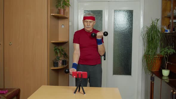 Senior Elderly Mature Man Watching Online Distance Workout Exercises with Dumbbells on Mobile Phone