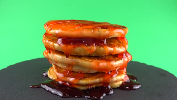 Pancakes with strawberry topping on a green background. Pancake lies on a black slate round stone.