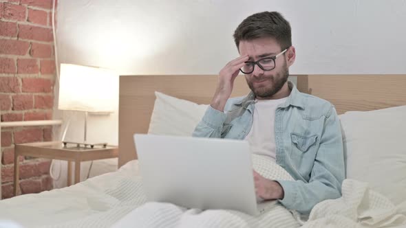 Young Male Designer Working on Laptop and Having Headache in Bed