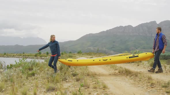 Caucasian couple having a good time on a trip to the mountains, holding a kayak and walking towards