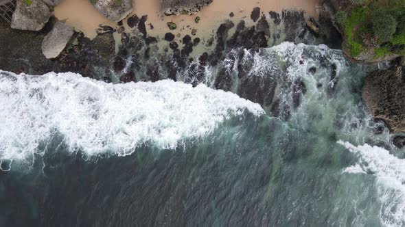 Top down aerial view of giant ocean waves crashing and foaming in coral beach