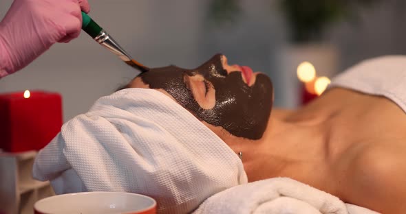 Young Woman Applies Detoxifying Clay Mask to Face in Beauty Salon