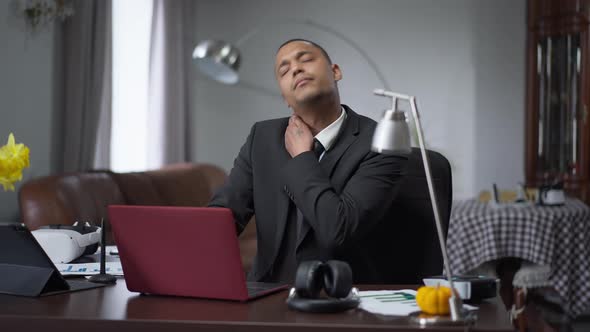 African American Young Man Stretching Neck Sitting at Table in Home Office Indoors