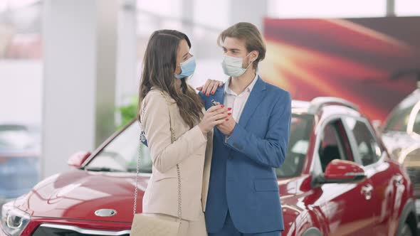 Happy Young Caucasian Couple in Covid19 Face Masks Bragging Car Keys in Dealership