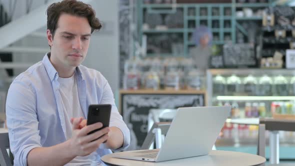 Creative Man with Laptop Using Smartphone in Cafe