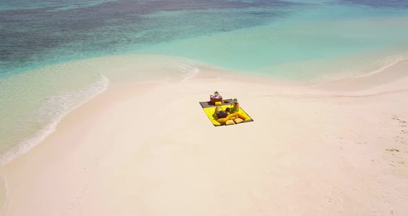 Aerial drone view of a man and woman couple having a picnic meal on a tropical island beach.