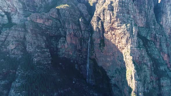 Aerial - Ascending drone with camera tilting down revealing waterfall falling down imposing cliff fa