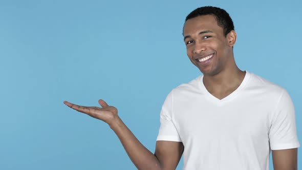 African Man Showing Product at Side Blue Background