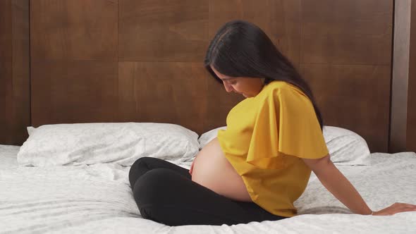 a young pregnant latinx woman sitting on bed