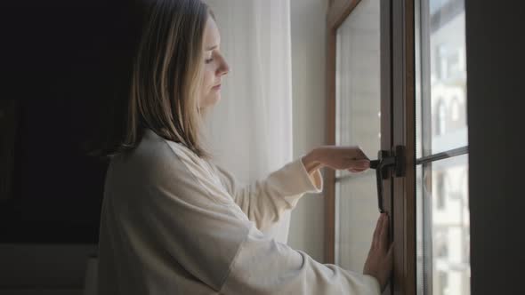 Relaxed Girl in Bathrobe Moves Curtains and Opens Window