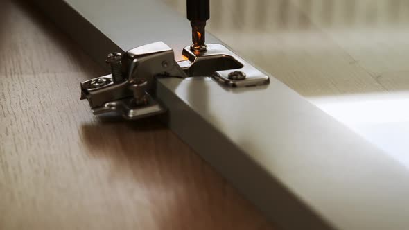 Close up of a drill screwing in a screw into a hinge for a glass cabinet.