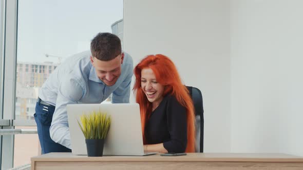 Businesspeople Discussing Projects on Laptop in Office. Girl with Red Hair and Caucasian Nationality