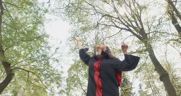 Attractive Young Lady Smiling Wearing Graduation Gown Throwing Mortarboard in Park