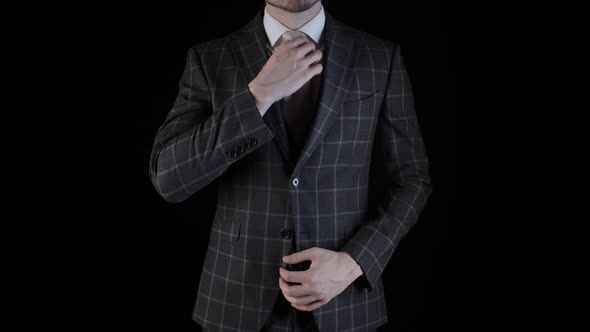 Handsome Businessman Wearing Suit Straightens His Necktie with Hand Isolated on Black Background