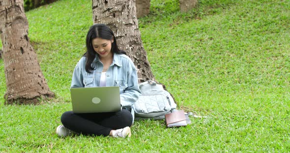 Woman Sitting On Grass In Park And Using Laptop Computer