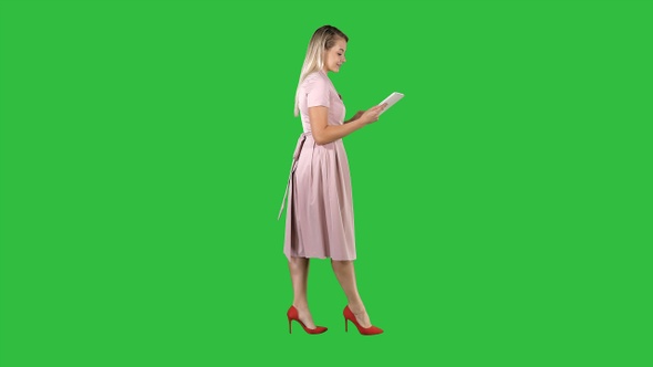 Blonde in pink dress walking and using tablet on a Green