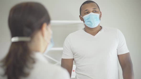 Serious African American Man in Face Mask Listening To Caucasian Woman and Shaking Head Gesturing