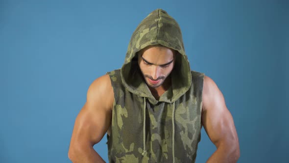 Bodybuilder in Camouflage Hoodie Flexing Biceps Muscles and Chests, Studio Shot