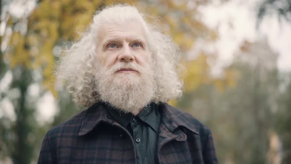 Closeup Portrait of Happy Cheerful Senior Man with Beard and Long Grey Hair Throwing Up Apple