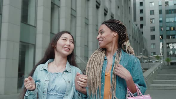 Two Beautiful Asian and African Girls Have Fun Walking Down the Street with Their Purchases After