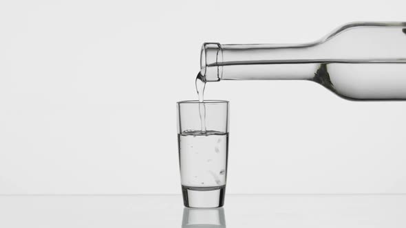 Pouring Up Shot of Vodka From a Bottle Into Glass. White Background