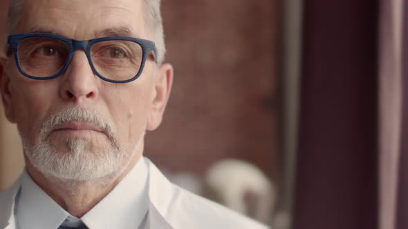 Grayhaired Mature Man in Blue Glasses Wearing a Medical Robe and a Gray Beard