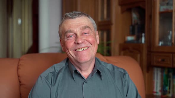 Slow motion close up shot of senior man looking at camera smiling at home indoors