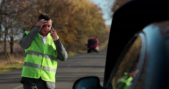 Portrait of Young Man in a Safety Vest Standing in Front of His Broken Car Looking at Car Engine and