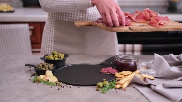 Woman Puts Slices of Fuet Sausage Onto Stone Serving Board at Domestic Kitchen