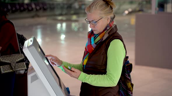 Pretty, mature woman holding smartphone and doing a self check in at the airport.