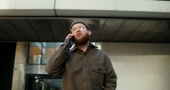 A Young Man is Typing on a Mobile Phone While Walking Around the Business Center