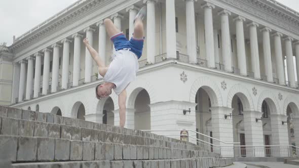 Wide Shot of Confident Break Dancer Moving Legs Up As Standing on One Hand. Portrait of Athletic