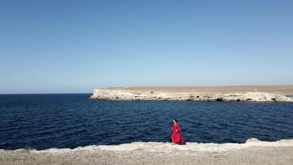 Brunette Woman in a Red Long Dress Walk on the Edge of a Cliff By the Sea