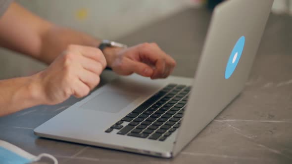 Young Man Finishes Typing on Laptop Puts on Medical Face Mask and Walks Away