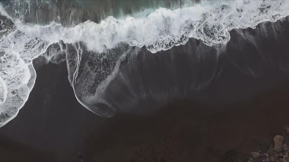 Aerial view of volcanic beach cove seashore with black sand. Beautiful contrast with waves white foa