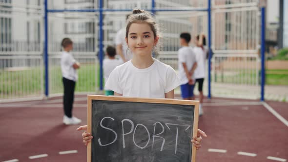 Portrait of Little Cute School Girl Standing Holding the Chalkboard Sport and Looking at the Camera