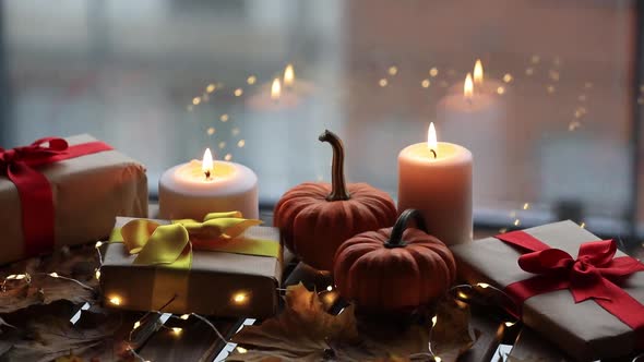 Gift, candles and pumpkin on wooden table with fairy lights