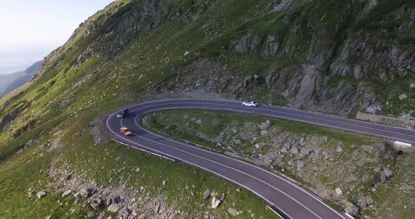 White car driving around hairpin turn on high altitude alpine road on descent
