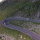 White car driving around hairpin turn on high altitude alpine road on descent - VideoHive Item for Sale