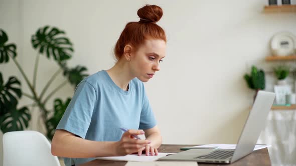 Serious Young Woman Accountant Is Taking Notes in Documents, Working on Laptop.