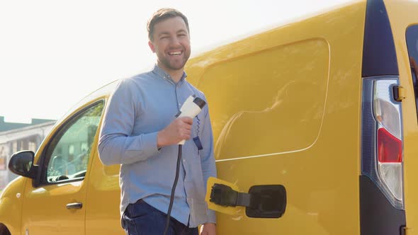 A Happy Man with a Charger at a Charging Station