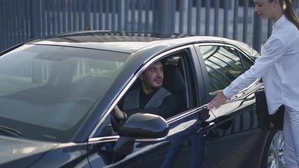 Young Slim Woman Closing Car Door for Man Walking Away Passing Camera