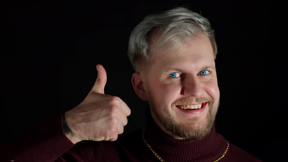 Smiling Man in Stylish Blouse Looking Approvingly at Camera Showing Thumbs Up on Black Background