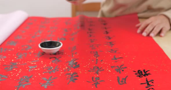 Asian man writing chinese calligraphy on red paper